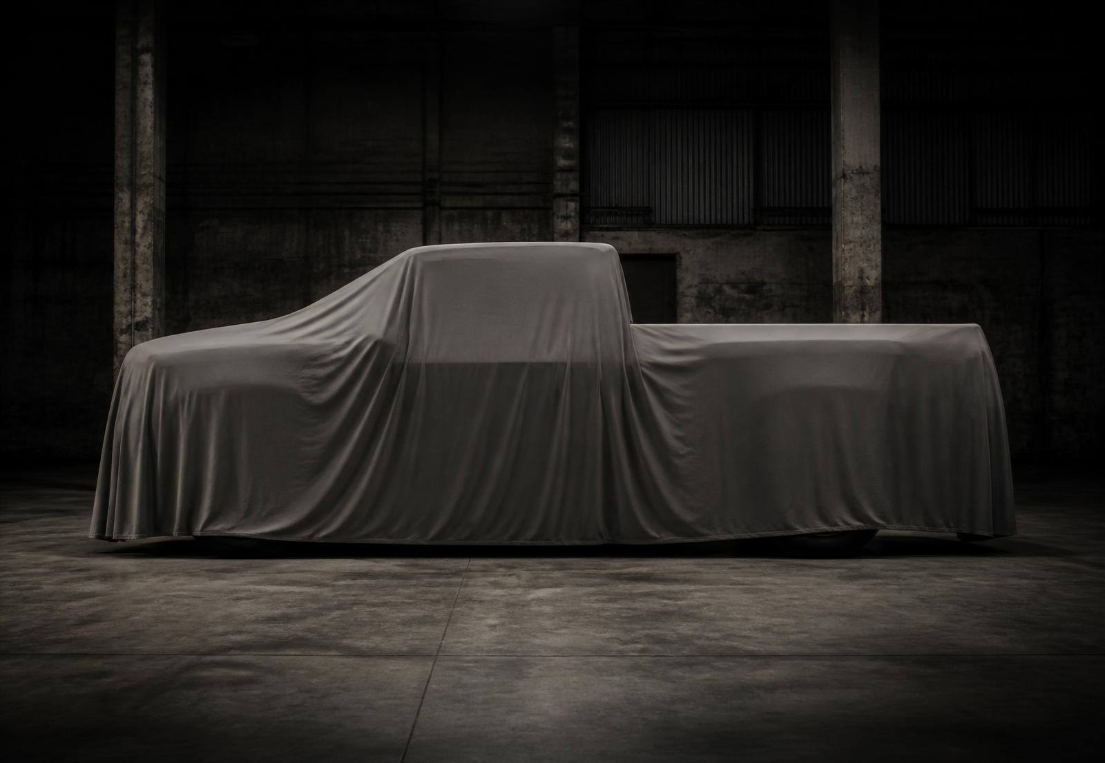 A pickup truck prototype fully concealed beneath a matte cover in a dark industrial hall