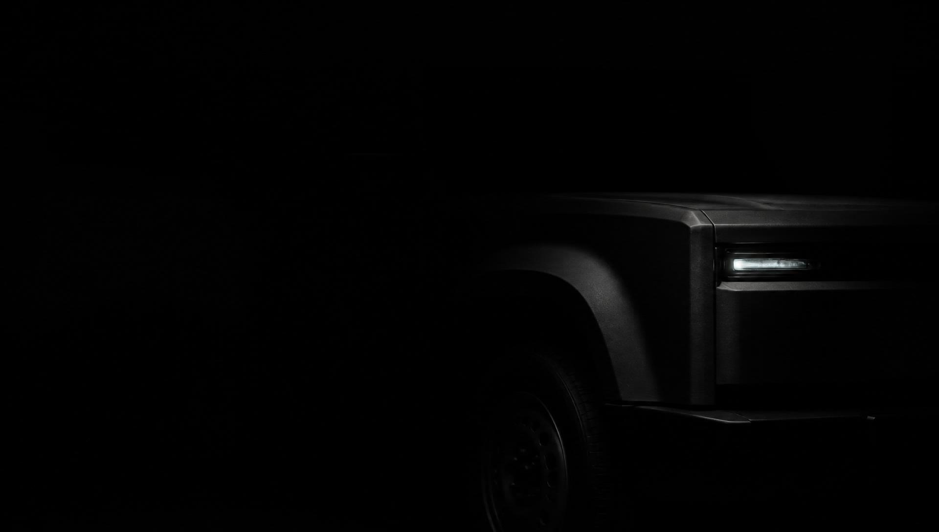 A boxy truck front corner emerging from near-total darkness, lit by a single slim headlight